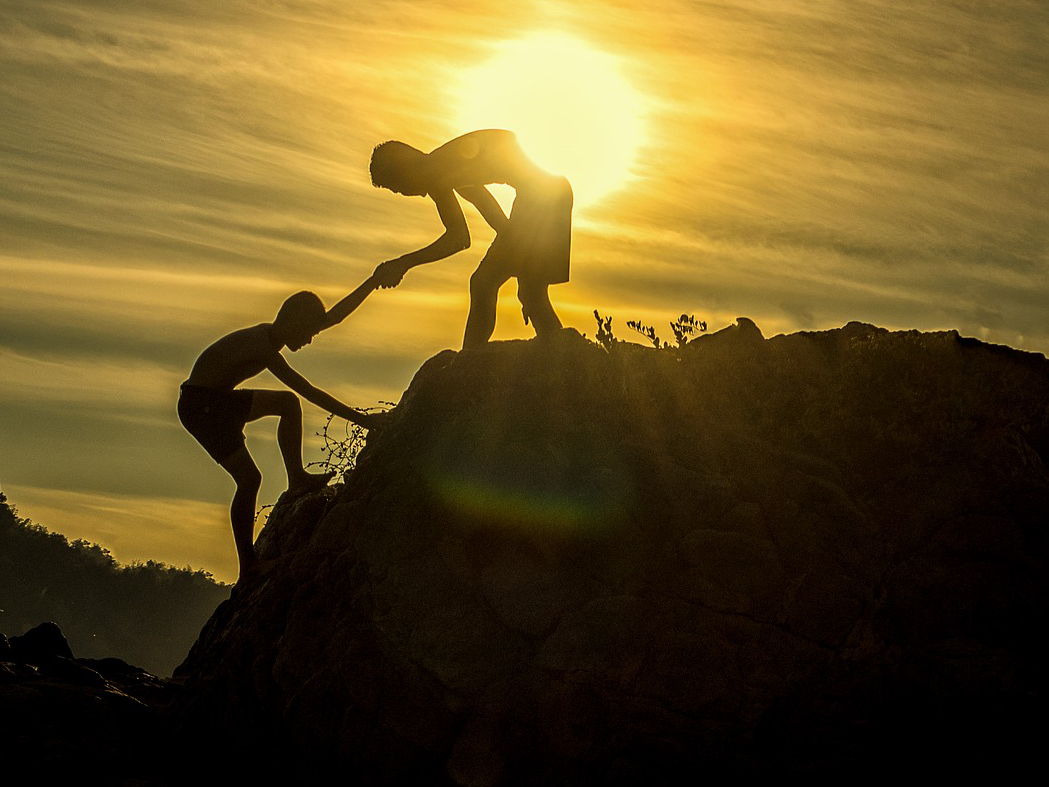 Two boys climbing a mountain with the sun behind them