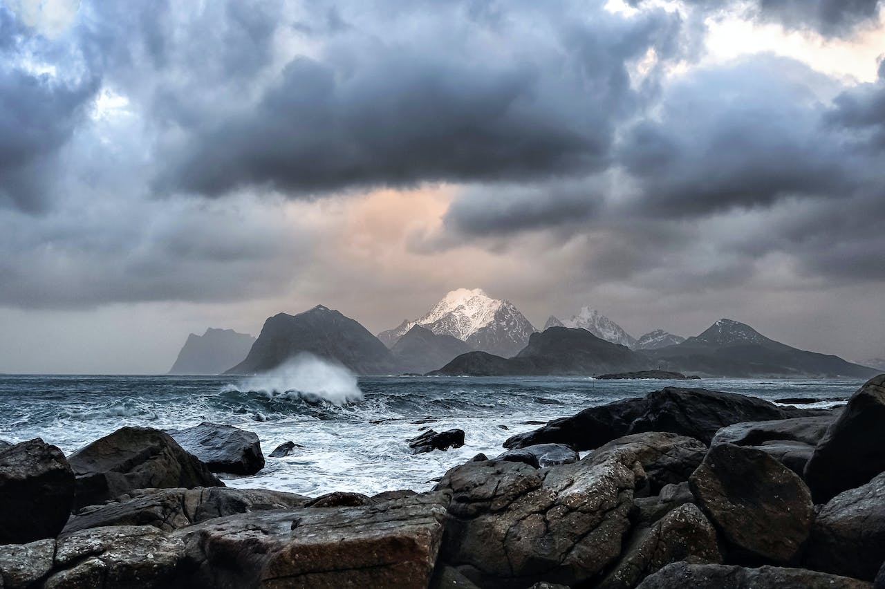 Dramatic sea scene with waves crashing against rocks with snowy mountains