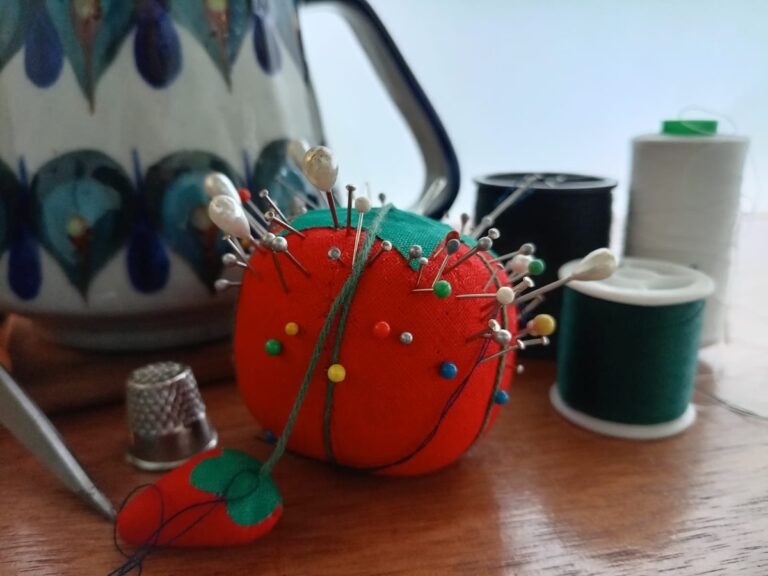 a red pincushion, spools of thread, an artisanal mug, and a thimble artfully arranged on a wooden desk.