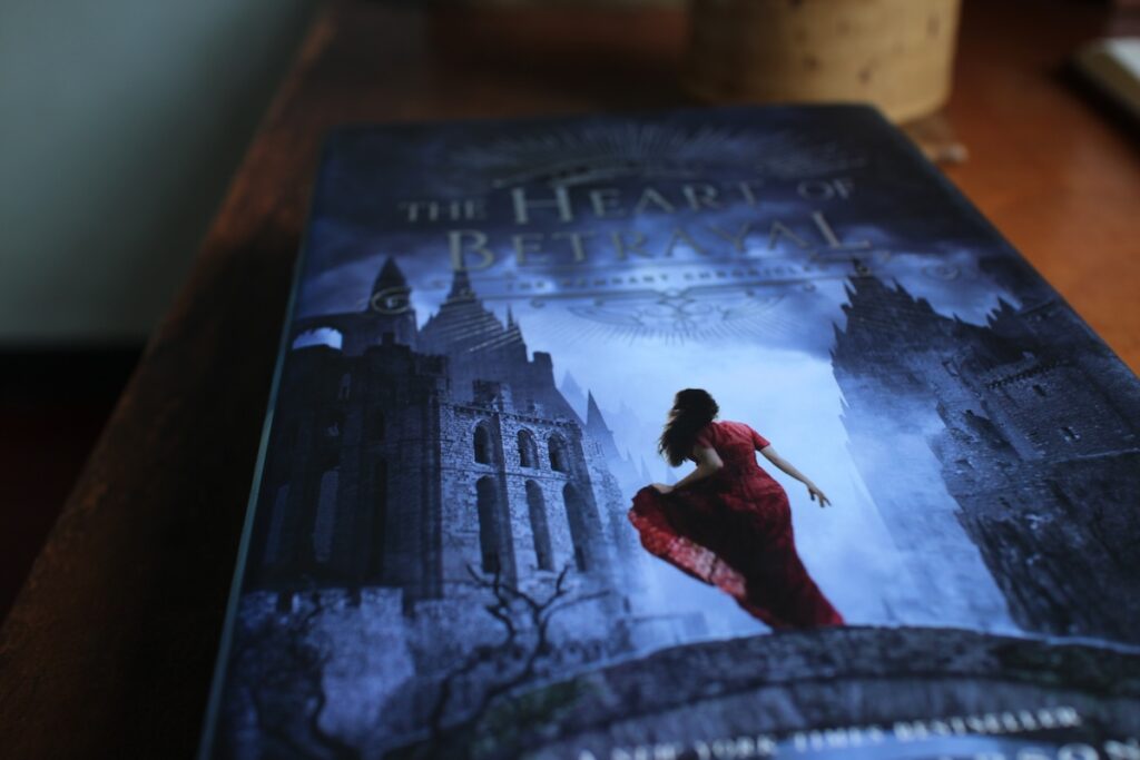 A woman in a red dress stands on a stone bridge looking toward a mysterious castle.