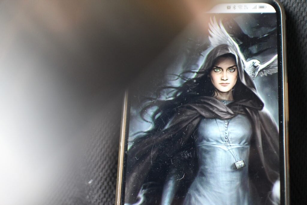 A woman in a dark cloak with startling green eyes glares into the camera, while the left side of the image is obscured by the metallic blur of a knife. This is part of the cover of "Vespertine" by Margaret Rogerson.